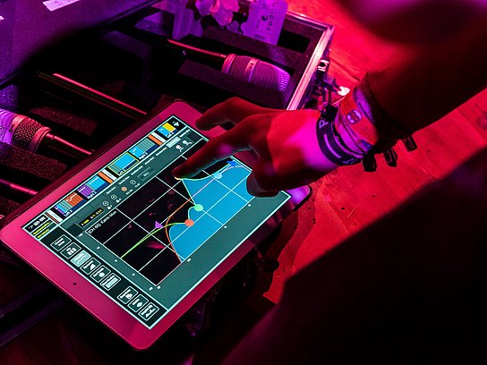 Ein Finger zeigt auf ein Tablet, dahinter liegen Mikrofone