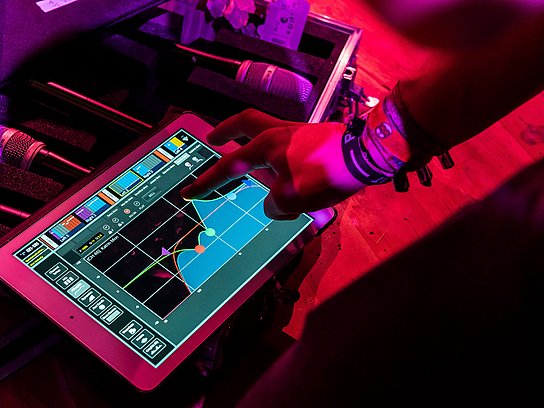 Ein Finger zeigt auf ein Tablet, dahinter liegen Mikrofone