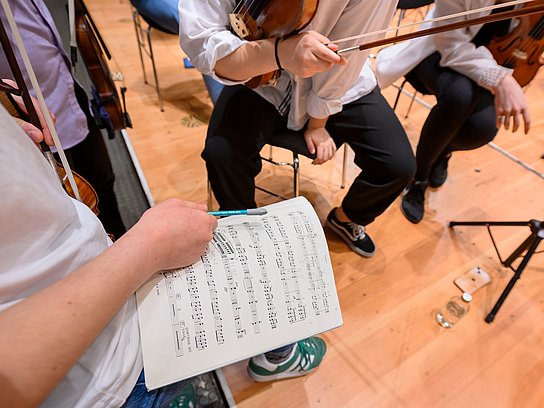 Ausschnitt aus einem Orchester, Person hält Bleistift und Notenblatt in der Hand