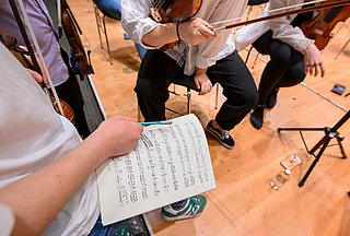 Ausschnitt aus einem Orchester, Person hält Bleistift und Notenblatt in der Hand