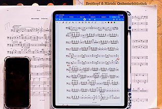 Aufgeschlagenes Notenblatt, darauf liegt ein Handy und ein Tablet