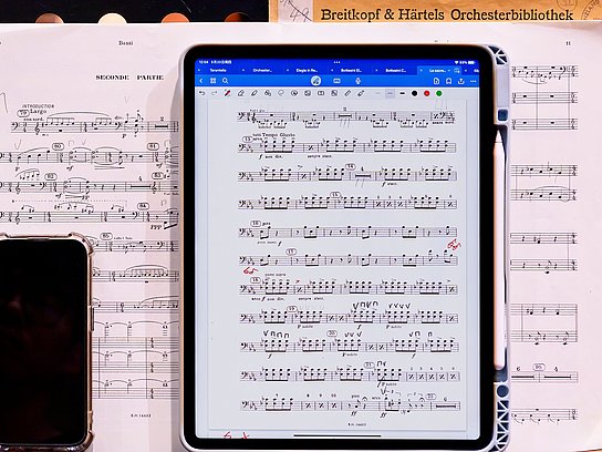 Aufgeschlagenes Notenblatt, darauf liegt ein Handy und ein Tablet