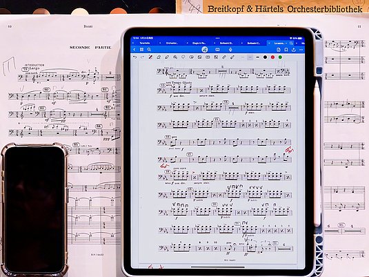 Aufgeschlagenes Notenblatt, darauf liegt ein Handy und ein Tablet