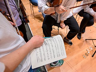 Ausschnitt aus einem Orchester, Person hält Bleistift und Notenblatt in der Hand